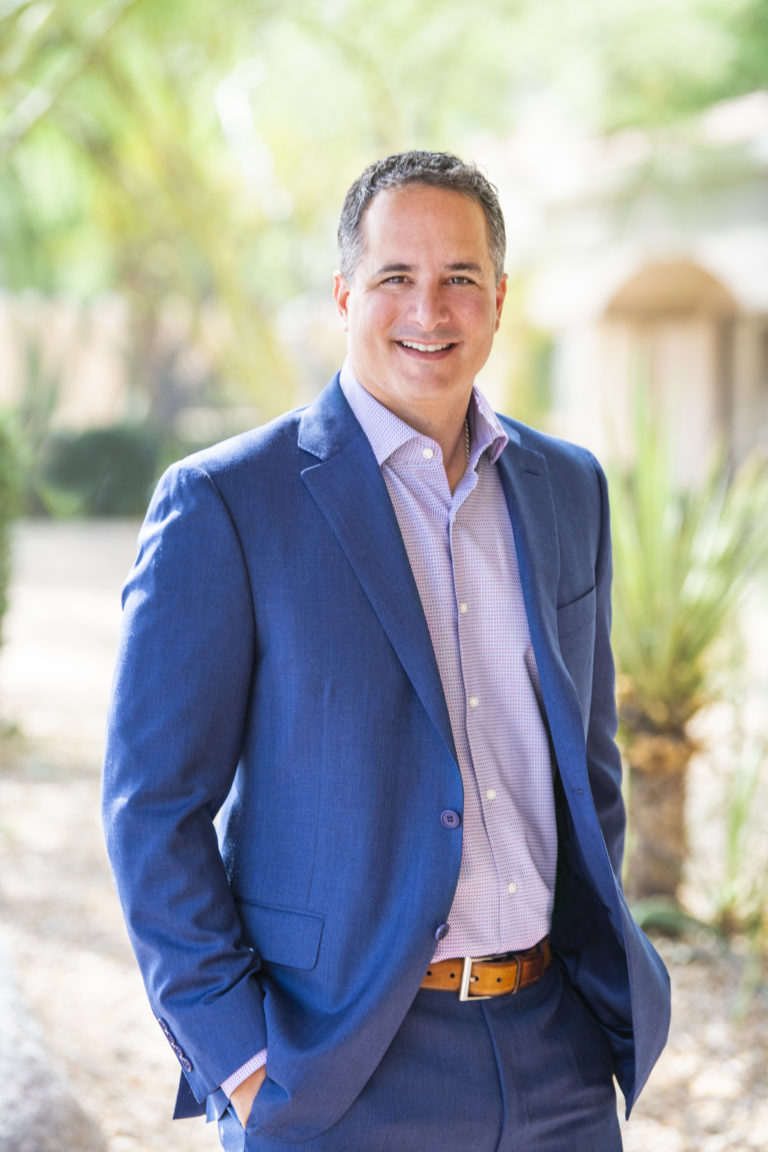 A man in a blue suit smiling in front of bushes representing the MegaPlanIT management team.