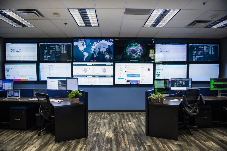 A managed security control room at MegaPlanIT with several monitors and desks.