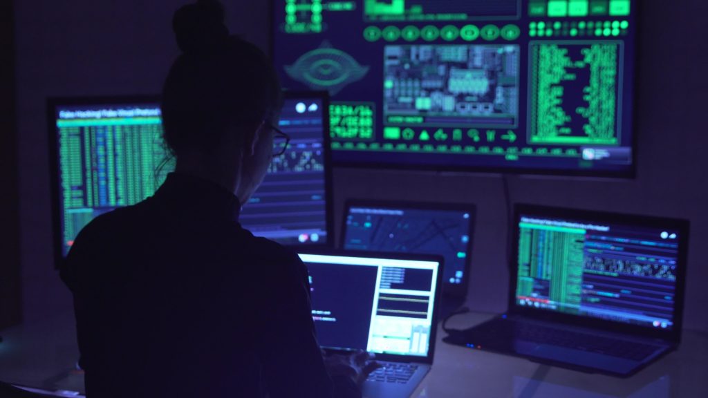 A woman is conducting vulnerability scanning on a computer in a dark room.