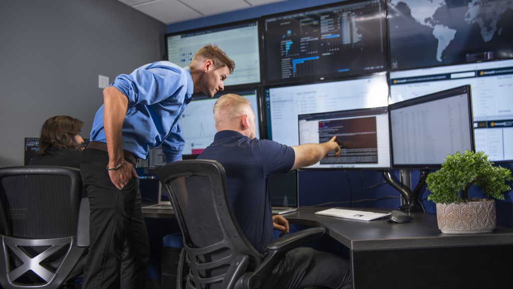 A man is pointing at a computer screen displaying cyber security details.