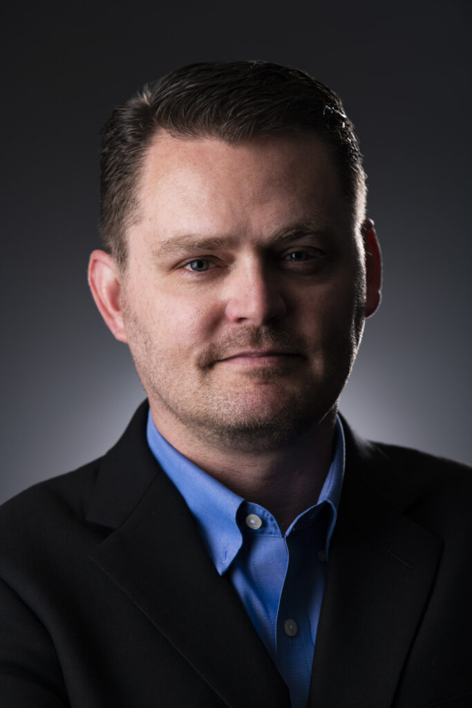 A man in a suit and blue shirt is posing for a photo to meet PCI Compliance standards.