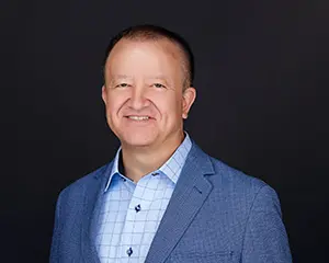 Frank Nudo, CHIEF OPERATING OFFICER at MegaplanIT in a blue suit leading a management team poses against a black background.